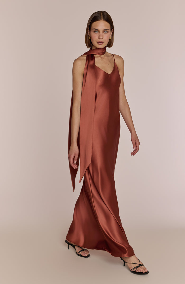 Woman wearing a rust-colored satin halter neck dress on a beige background