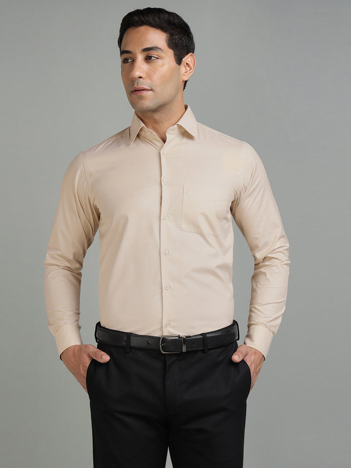 Man wearing a beige dress shirt and black pants against a gray background