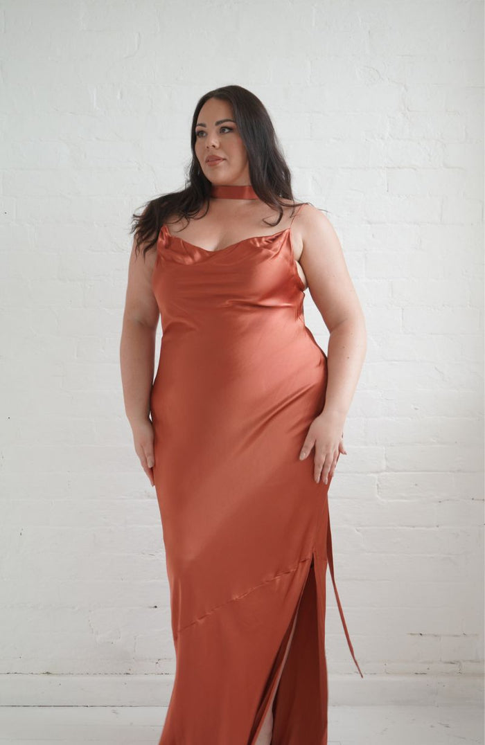 Woman wearing a rust-colored satin dress against a white brick wall.