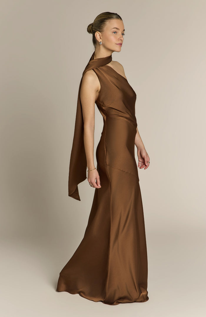 Woman wearing a brown evening gown with a cape on a plain background