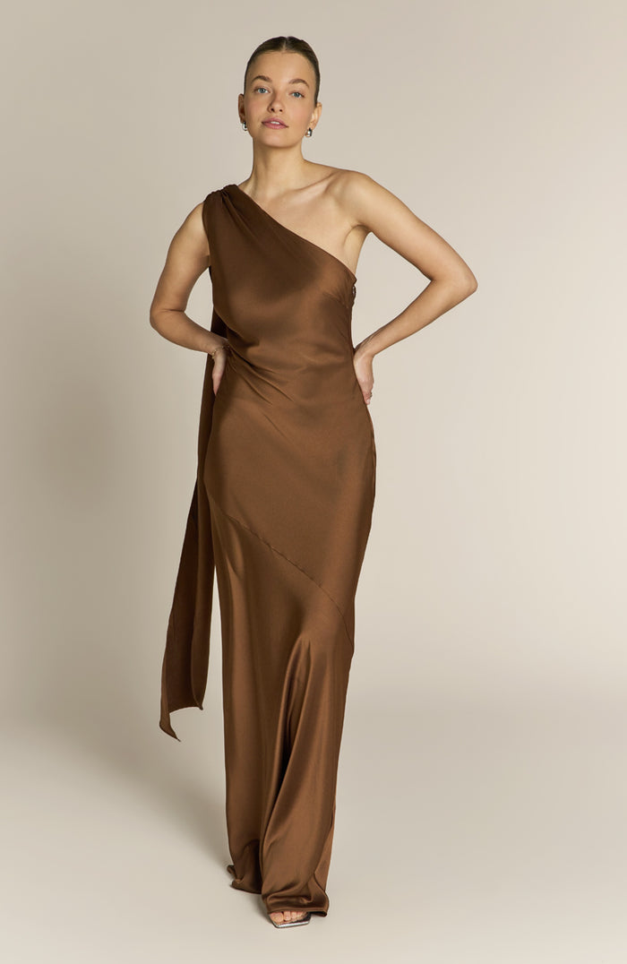 Woman wearing a brown one-shoulder dress against a beige background