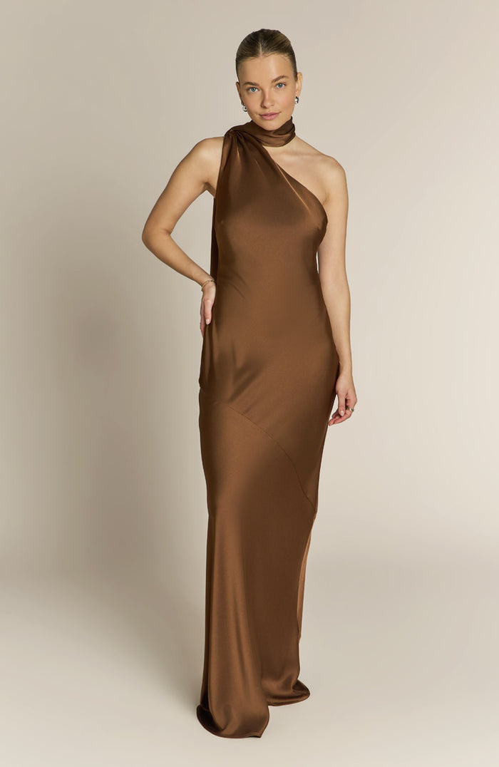 Woman wearing a brown one-shoulder evening gown against a plain background